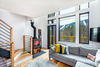 Ejemplo de sala de estar abierta rural con paredes blancas, suelo de madera en tonos medios, estufa de leña y televisor colgado en la pared