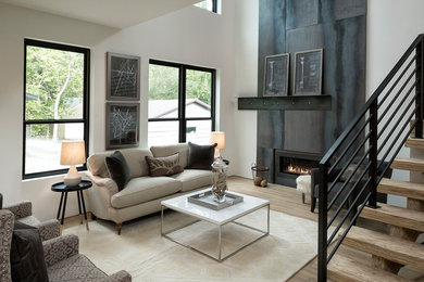 Imagen de sala de estar abierta industrial de tamaño medio sin televisor con paredes blancas, suelo de madera clara, chimenea lineal, marco de chimenea de metal, suelo beige y alfombra