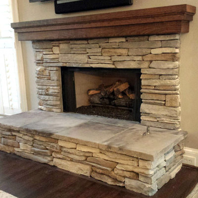 Inspiration for a rustic dark wood floor and brown floor family room remodel in Atlanta with a standard fireplace, a stone fireplace, beige walls and a wall-mounted tv