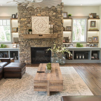 Inspiration for a large rustic open concept dark wood floor and brown floor family room remodel in Charleston with beige walls, a standard fireplace, a stone fireplace and a wall-mounted tv