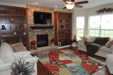 Example of a mid-sized classic enclosed medium tone wood floor family room design in St Louis with white walls, a standard fireplace, a stone fireplace and a wall-mounted tv