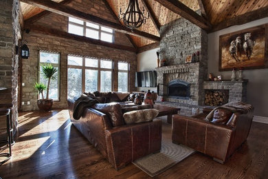 Inspiration for a large southwestern open concept medium tone wood floor family room remodel in Toronto with gray walls, a standard fireplace, a stone fireplace and a wall-mounted tv