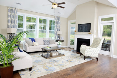 Modelo de sala de estar abierta tradicional con paredes beige, suelo de madera en tonos medios, todas las chimeneas y televisor colgado en la pared