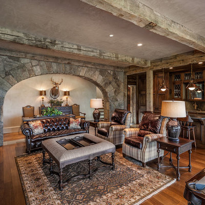 Example of a large tuscan open concept medium tone wood floor and brown floor family room design in Other with gray walls, a standard fireplace, a stone fireplace and a wall-mounted tv