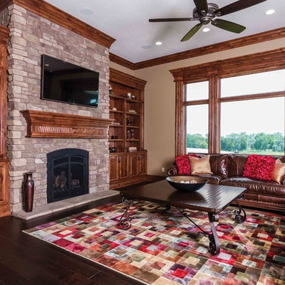 Example of a classic dark wood floor family room design in Other with beige walls, a standard fireplace, a stone fireplace and a wall-mounted tv