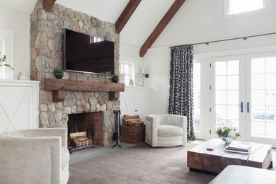 Modelo de sala de estar abierta tradicional grande con paredes blancas, todas las chimeneas, marco de chimenea de piedra, televisor colgado en la pared y suelo marrón