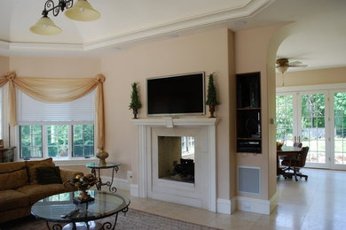На фото: гостиная комната в классическом стиле с бежевыми стенами, двусторонним камином и телевизором на стене