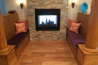 Imagen de sala de estar tradicional con paredes beige, suelo de madera en tonos medios, chimenea de doble cara y marco de chimenea de piedra
