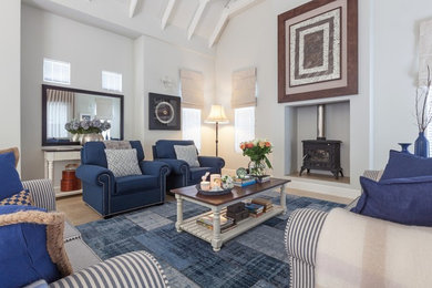 Ejemplo de sala de estar de estilo de casa de campo con paredes blancas, suelo de madera clara, estufa de leña, marco de chimenea de yeso y suelo beige