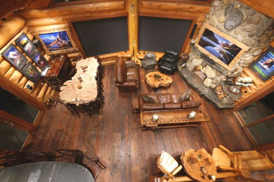Ejemplo de sala de estar abierta rural de tamaño medio con paredes marrones, suelo de madera oscura, estufa de leña, marco de chimenea de piedra y televisor retractable