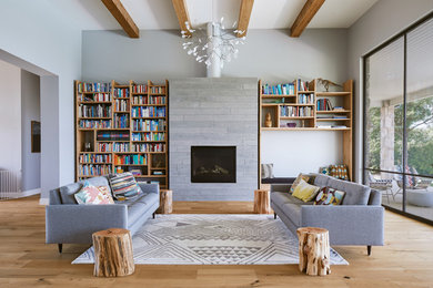 Moderne Bibliothek mit grauer Wandfarbe, hellem Holzboden, Kamin und Kaminumrandung aus Beton in Austin