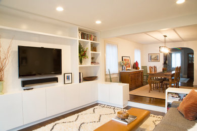 Inspiration for a mid-sized modern enclosed medium tone wood floor and brown floor family room remodel in New York with white walls and a wall-mounted tv