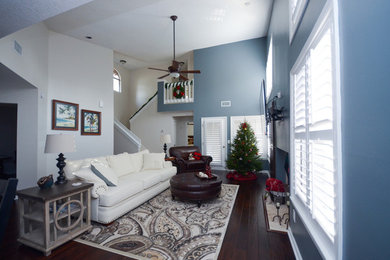 Modelo de sala de estar abierta tradicional de tamaño medio sin chimenea con paredes azules, suelo de madera oscura y televisor colgado en la pared