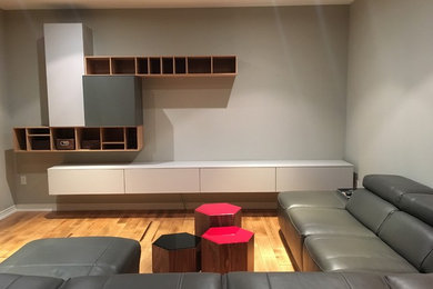 Imagen de sala de estar actual con paredes grises, suelo de madera clara y pared multimedia