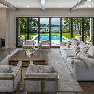 Geräumiges, Offenes Modernes Wohnzimmer mit weißer Wandfarbe, braunem Holzboden, braunem Boden, Kaminumrandung aus Holzdielen, Wand-TV und freigelegten Dachbalken in Tampa