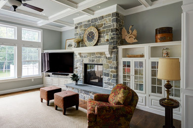 Diseño de sala de estar abierta clásica grande con paredes grises, suelo de madera en tonos medios, chimenea de doble cara, marco de chimenea de piedra, pared multimedia y suelo marrón