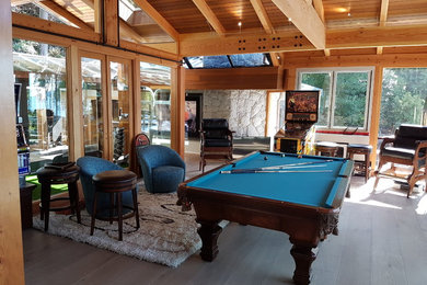Example of a mid-sized arts and crafts open concept light wood floor and beige floor game room design in Vancouver with white walls, a standard fireplace, a stone fireplace and a wall-mounted tv