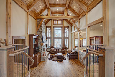 Example of a mountain style medium tone wood floor family room design in Calgary with beige walls, a standard fireplace, a stone fireplace and a media wall