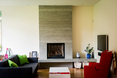 Imagen de sala de estar abierta moderna grande con paredes blancas, suelo de madera en tonos medios, todas las chimeneas y marco de chimenea de hormigón