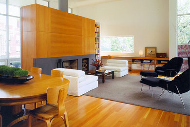 Imagen de sala de estar con biblioteca abierta moderna grande con paredes blancas, suelo de madera en tonos medios, todas las chimeneas y marco de chimenea de piedra
