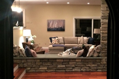 Imagen de sala de estar abierta tradicional renovada grande con paredes beige, suelo de madera en tonos medios, chimenea de esquina, marco de chimenea de piedra y televisor colgado en la pared