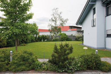 Exempel på en stor modern trädgård i full sol framför huset på sommaren, med en stödmur och marksten i betong