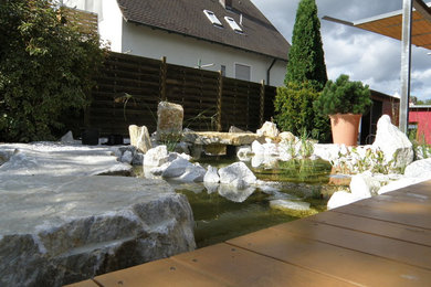 Imagen de jardín tradicional de tamaño medio en verano en patio trasero con fuente y exposición parcial al sol