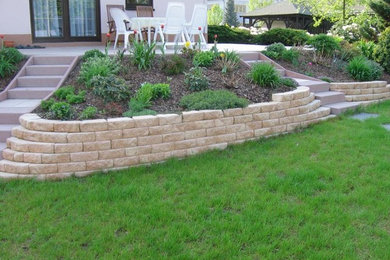 Classic sloped garden in Other with a retaining wall and natural stone paving.