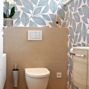 Design ideas for a mid-sized contemporary powder room in Dresden with beige tile, light wood cabinets, a wall-mount toilet, a drop-in sink, glass benchtops and multi-coloured walls.