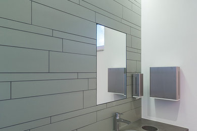 ケルンにある高級な中くらいなインダストリアルスタイルのおしゃれなトイレ・洗面所 (壁掛け式トイレ、緑のタイル、石タイル、白い壁、セラミックタイルの床、コンクリートの洗面台、一体型シンク) の写真