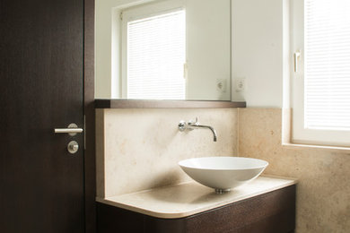 Photo of a medium sized contemporary cloakroom in Dusseldorf with flat-panel cabinets, dark wood cabinets, beige tiles, white walls, marble flooring, a vessel sink and stone slabs.