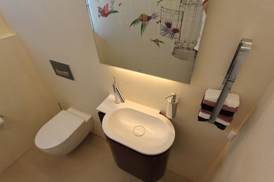 Idee per un bagno di servizio minimal di medie dimensioni con ante lisce, ante grigie, WC sospeso, piastrelle beige, pareti beige, pavimento in cemento, lavabo integrato, top in superficie solida e pavimento beige