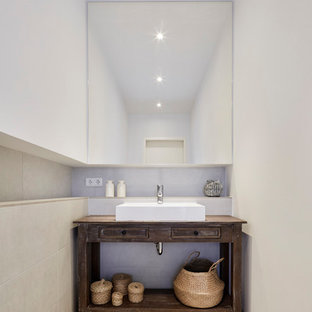 Kleine Urige Gästetoilette mit Schrankfronten mit vertiefter Füllung, dunklen Holzschränken, beigefarbenen Fliesen, Zementfliesen, weißer Wandfarbe, Keramikboden, Aufsatzwaschbecken, Waschtisch aus Holz, beigem Boden und brauner Waschtischplatte in Köln