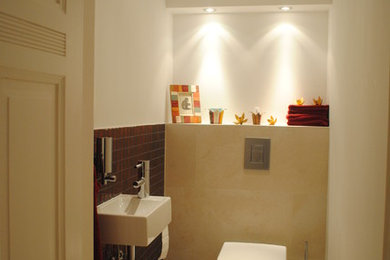 ベルリンにあるコンテンポラリースタイルのおしゃれなトイレ・洗面所 (壁掛け式トイレ、赤いタイル、モザイクタイル、白い壁、セラミックタイルの床、壁付け型シンク、ベージュの床) の写真