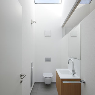 Mittelgroße Moderne Gästetoilette mit flächenbündigen Schrankfronten, hellbraunen Holzschränken, Wandtoilette mit Spülkasten, weißer Wandfarbe, integriertem Waschbecken und grauem Boden in München