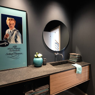 Mittelgroße Moderne Gästetoilette mit flächenbündigen Schrankfronten, schwarzer Wandfarbe, hellem Holzboden, integriertem Waschbecken, Granit-Waschbecken/Waschtisch, beigem Boden, schwarzer Waschtischplatte, eingebautem Waschtisch und hellbraunen Holzschränken in Sonstige