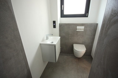 Moderne Gästetoilette mit Wandtoilette mit Spülkasten, grauen Fliesen, Keramikfliesen, grauer Wandfarbe, Einbauwaschbecken und grauem Boden in Sonstige