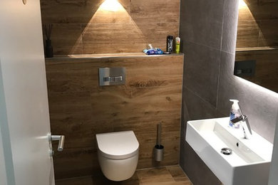 Kleine Urige Gästetoilette mit Wandtoilette mit Spülkasten, braunen Fliesen, schwarzen Fliesen, Wandwaschbecken und braunem Boden in Hannover