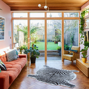 Retro games room in London with pink walls, medium hardwood flooring, a brick fireplace surround and a wall mounted tv.