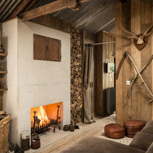 Imagen de sala de estar con biblioteca rústica con suelo de madera clara, chimenea tradicional, televisor retractable y marco de chimenea de hormigón