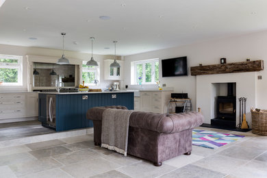 Large traditional open plan games room in Wiltshire with white walls, ceramic flooring, a wood burning stove, a stone fireplace surround, a wall mounted tv and grey floors.