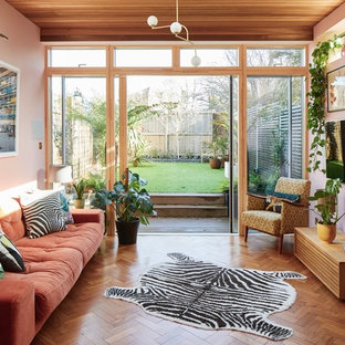 This is an example of a retro games room in Surrey with pink walls, medium hardwood flooring, a brick fireplace surround and a wall mounted tv.