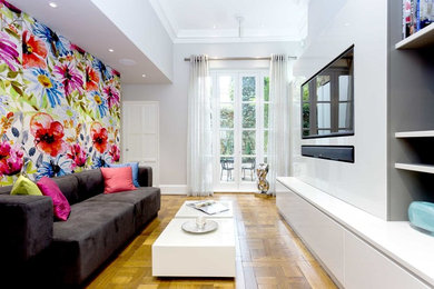 Imagen de sala de estar actual sin chimenea con suelo de madera clara, pared multimedia y paredes grises