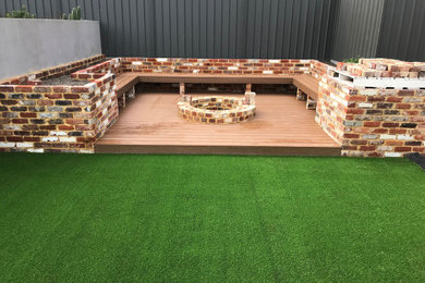 Inspiration pour un jardin arrière minimaliste avec un foyer extérieur, une exposition ensoleillée et une terrasse en bois.