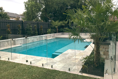 Modelo de piscina actual grande en patio trasero con adoquines de piedra natural