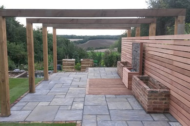 This is an example of a medium sized country back full sun garden for summer in Buckinghamshire with a retaining wall and natural stone paving.