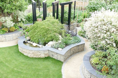 Inspiration for a medium sized modern back full sun raised pond for autumn in Hertfordshire with a retaining wall and natural stone paving.