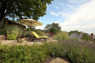 Réalisation d'un grand jardin à la française champêtre l'été avec un mur de soutènement, une exposition ensoleillée, une pente, une colline ou un talus et des pavés en pierre naturelle.