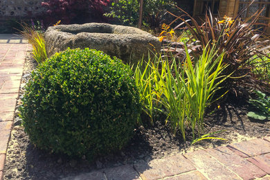 Diseño de jardín clásico en verano en patio con fuente, exposición total al sol y adoquines de ladrillo