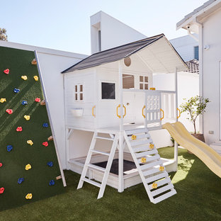 This is an example of a large beach style backyard garden for summer in Sydney with with outdoor playset.